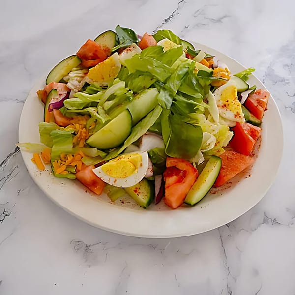 A fresh garden salad with lettuce, tomatoes, cucumbers, shredded cheese, and hard-boiled eggs.
